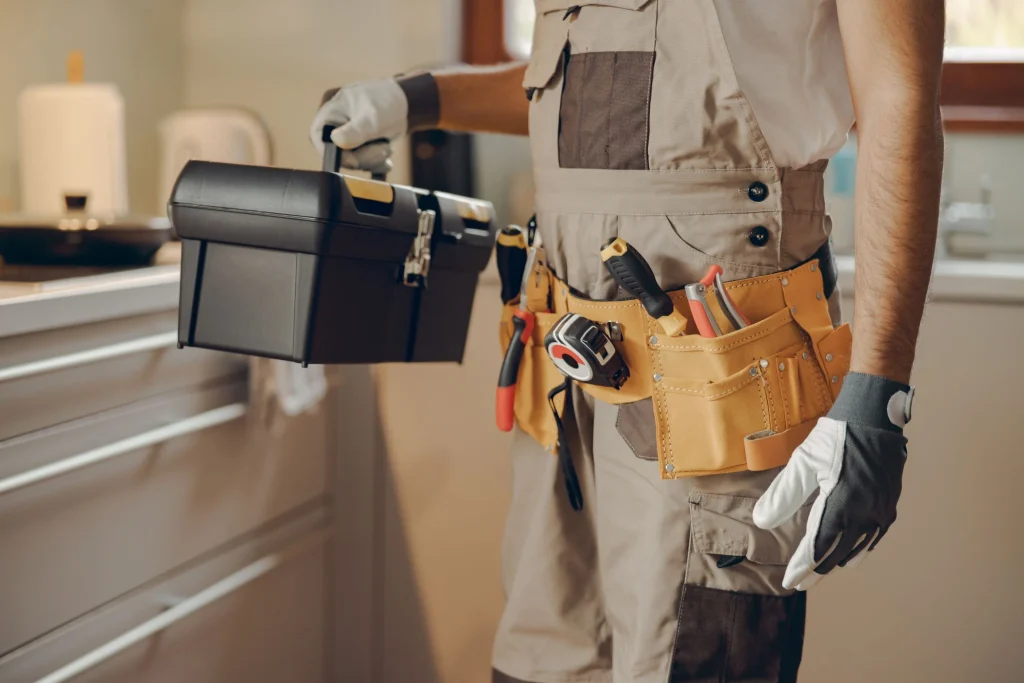 Professional handyman with tool belt and toolbox inside a home